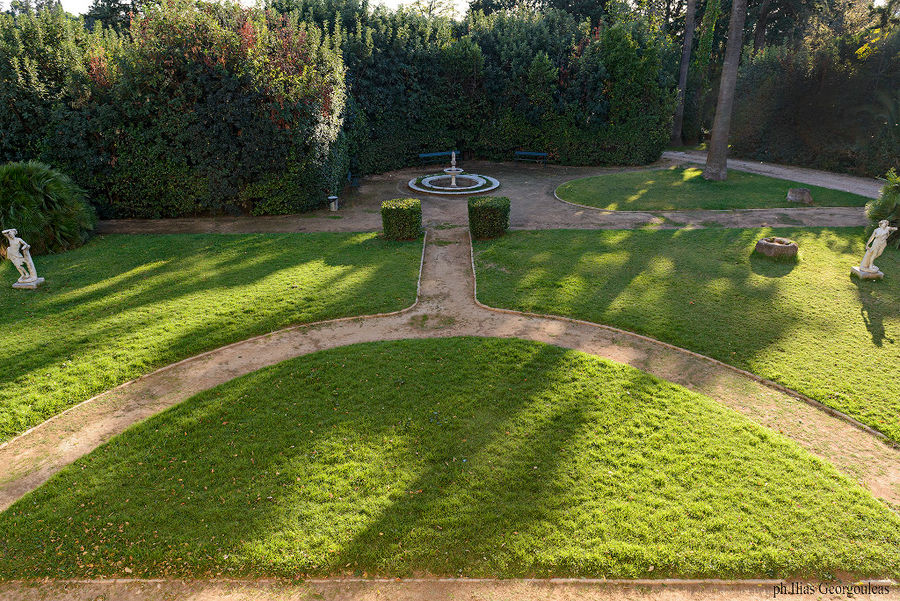 green lawns with stone alleys surrounding by trees at Pyrgos Vasilissis winery garden
